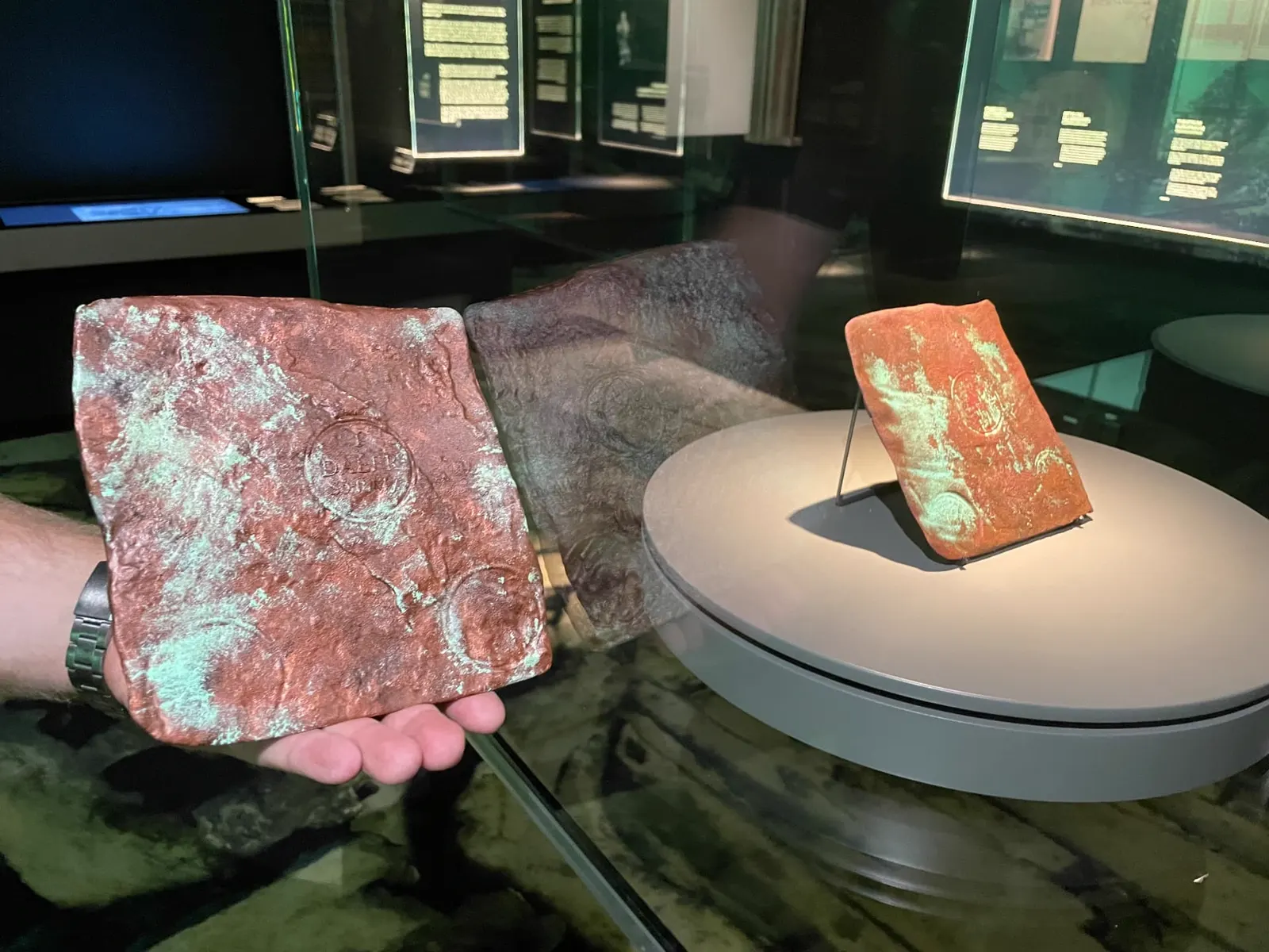 Återskapat kopparmynt hållet i handen framför montern på Vrak, Museum of Wrecks